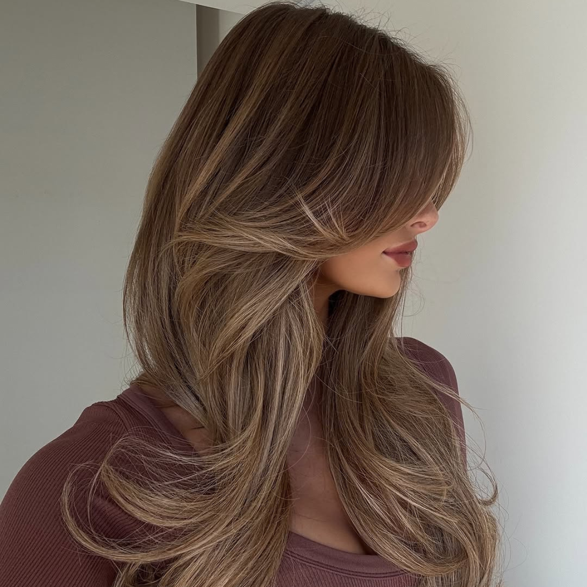 Side view of long layered bronde hair with warm highlights and contoured face-framing pieces.