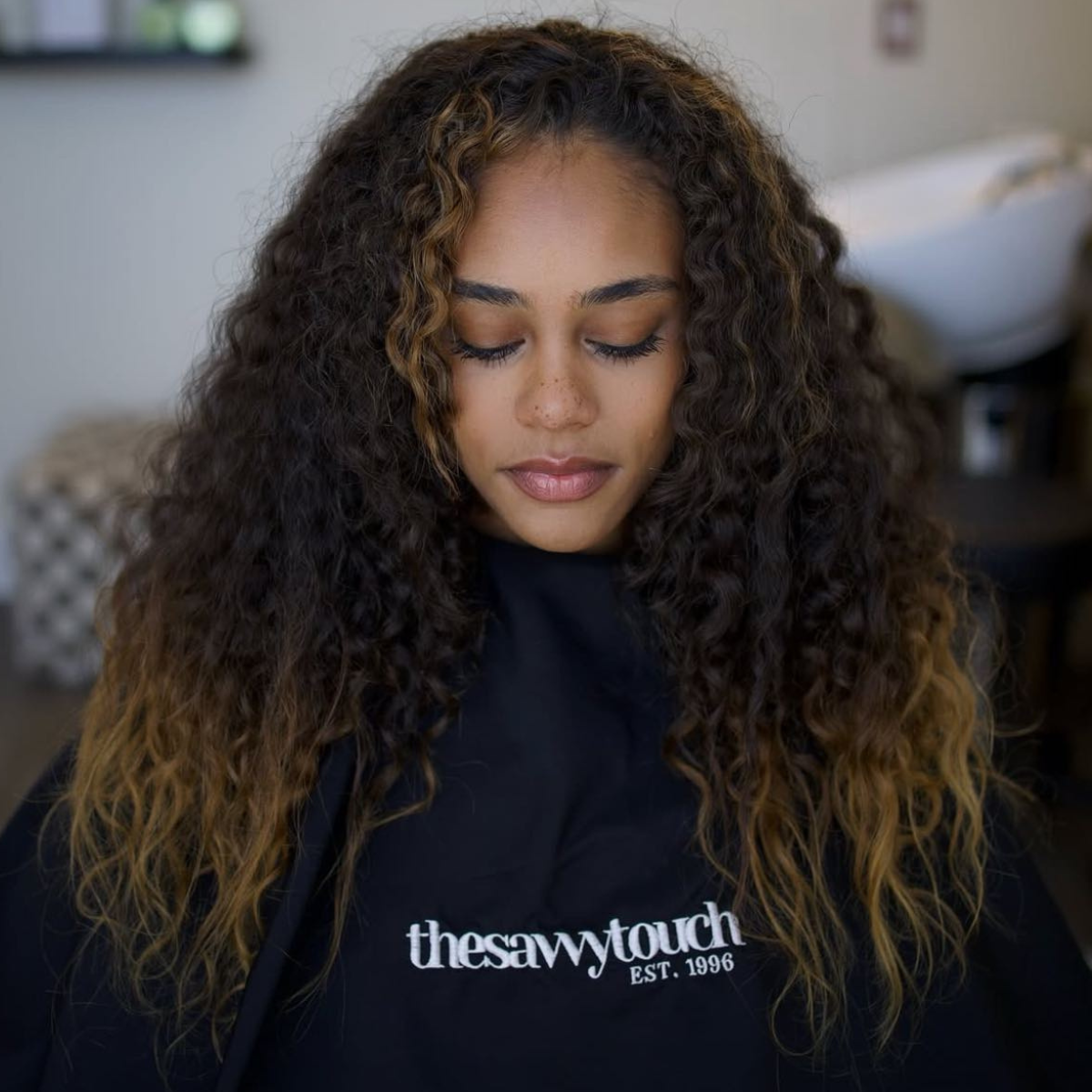 Before pic of curly brown-haired model wearing a salon cape