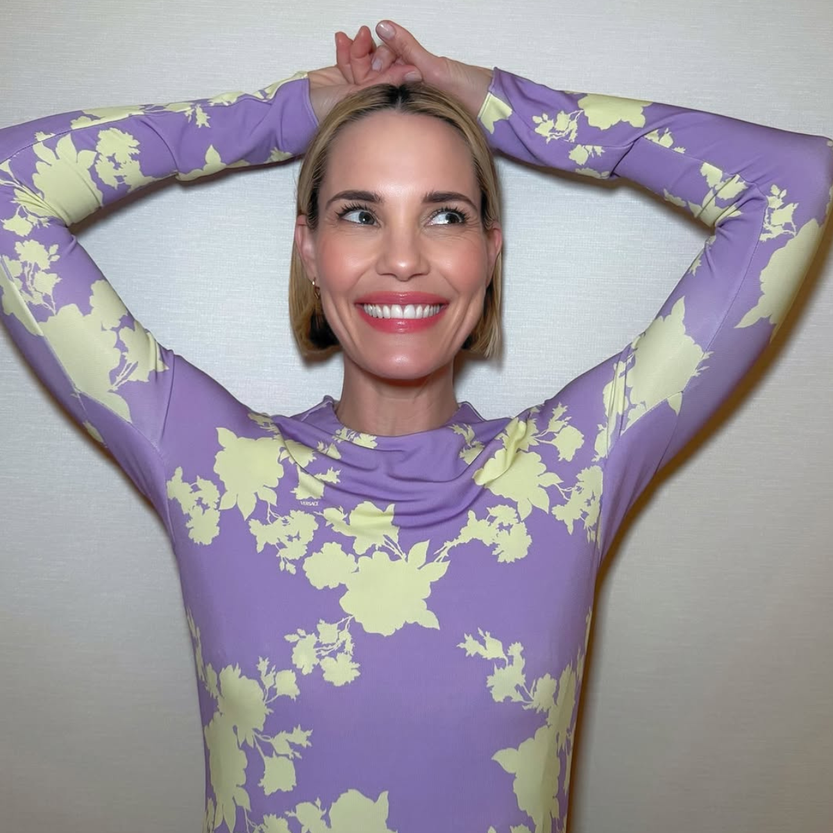 Leslie Bibb smiling in a lilac and yellow floral dress, showing off her crisp blonde bob