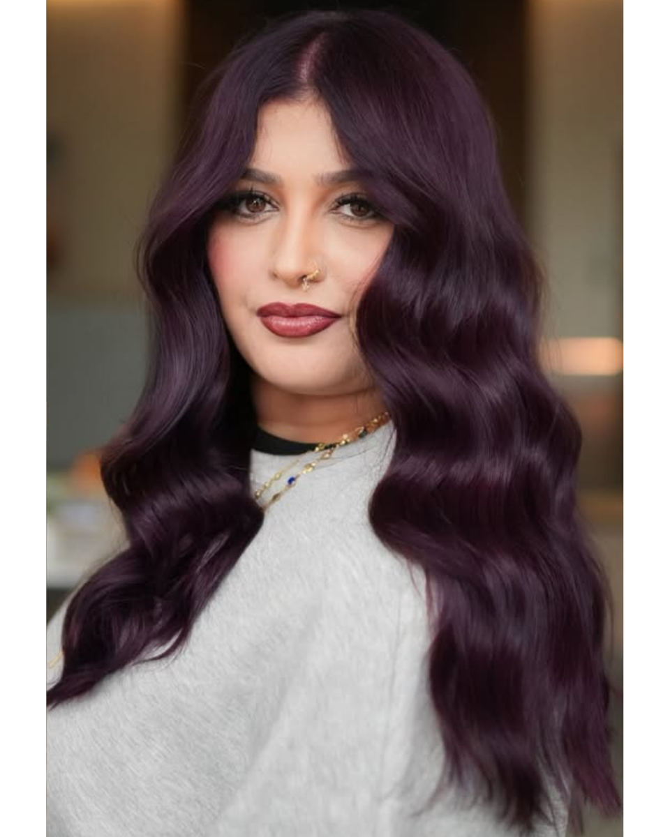 Close-up of finished long plum-purple hair color styled in soft, glossy waves with a center part.
